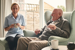 Senior man and female carer enjoying coffee at home