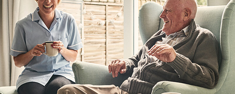 Senior man and female carer enjoying coffee at home